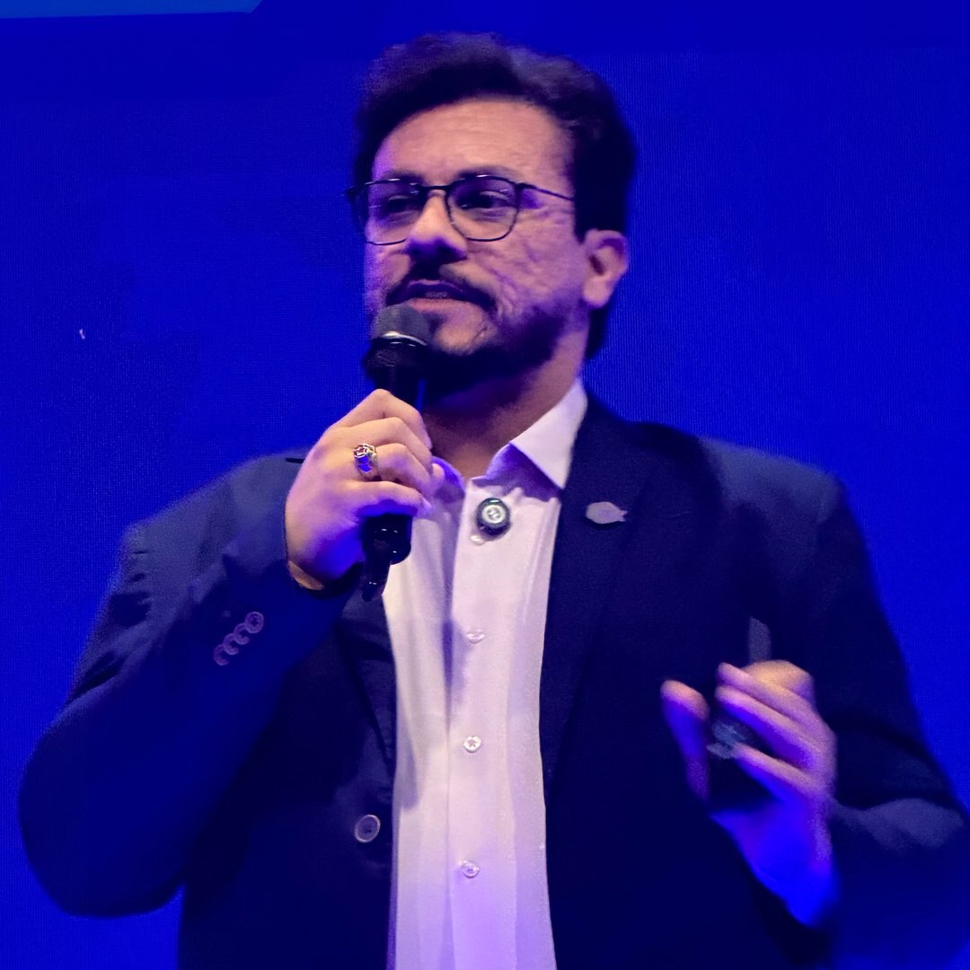 Itamar Vieira palestrando com microfone em um palco de iluminação azul